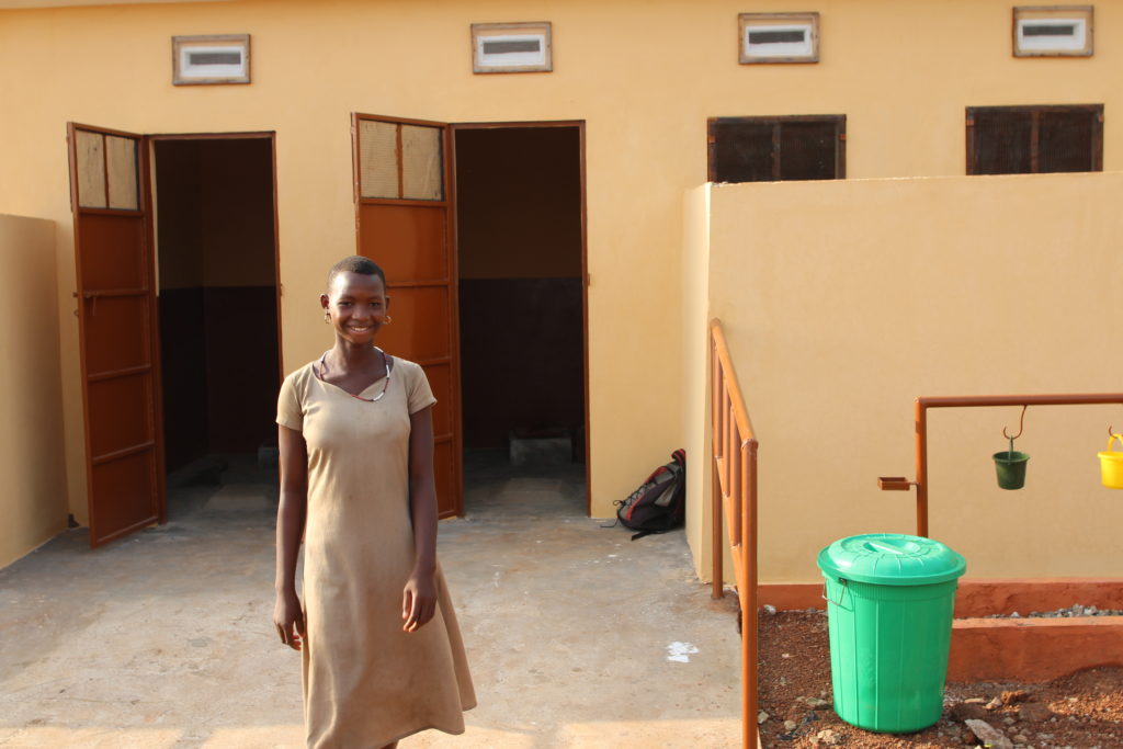 Girl standing in front of school latrines in Togo