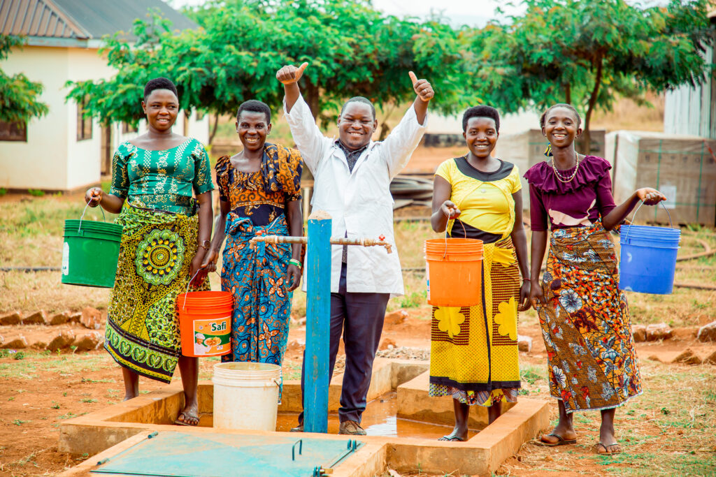 Dr. Boniface from Kigadye Health Center (Kigoma, Tanzania) posing for a photo with women who came to the health center to access clean and safe water brought by WASH facilities.