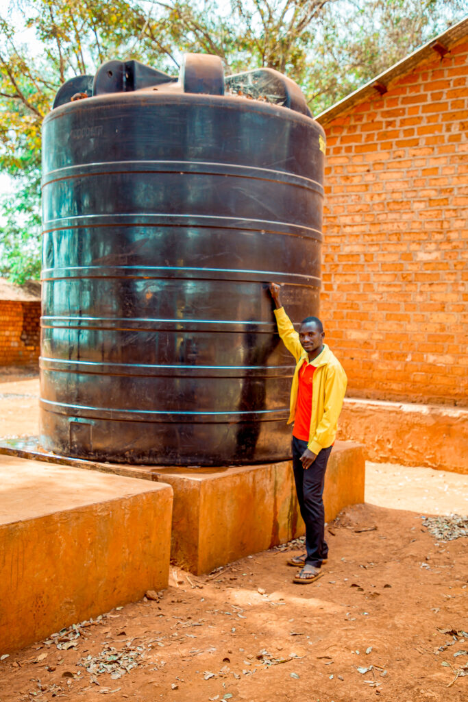 Headmaster of Kigeni Primary School in Kigoma, showing the school's water tank.