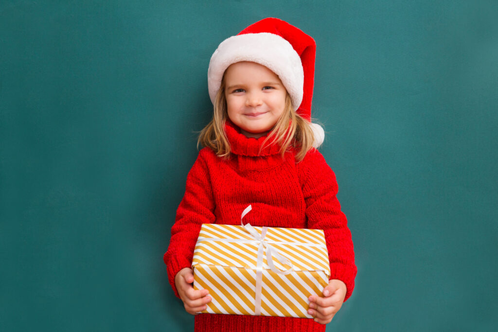 Child in a red sweater and a Santa hat with Christmas gift box.