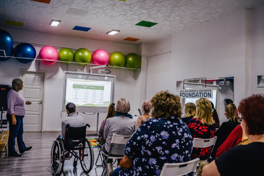 A group of people watchting a presentation taking place in a fitness room. One participant is in a wheelchair.