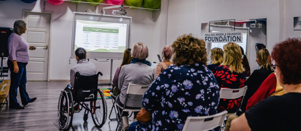 A group of people watchting a presentation taking place in a fitness room. One participant is in a wheelchair.